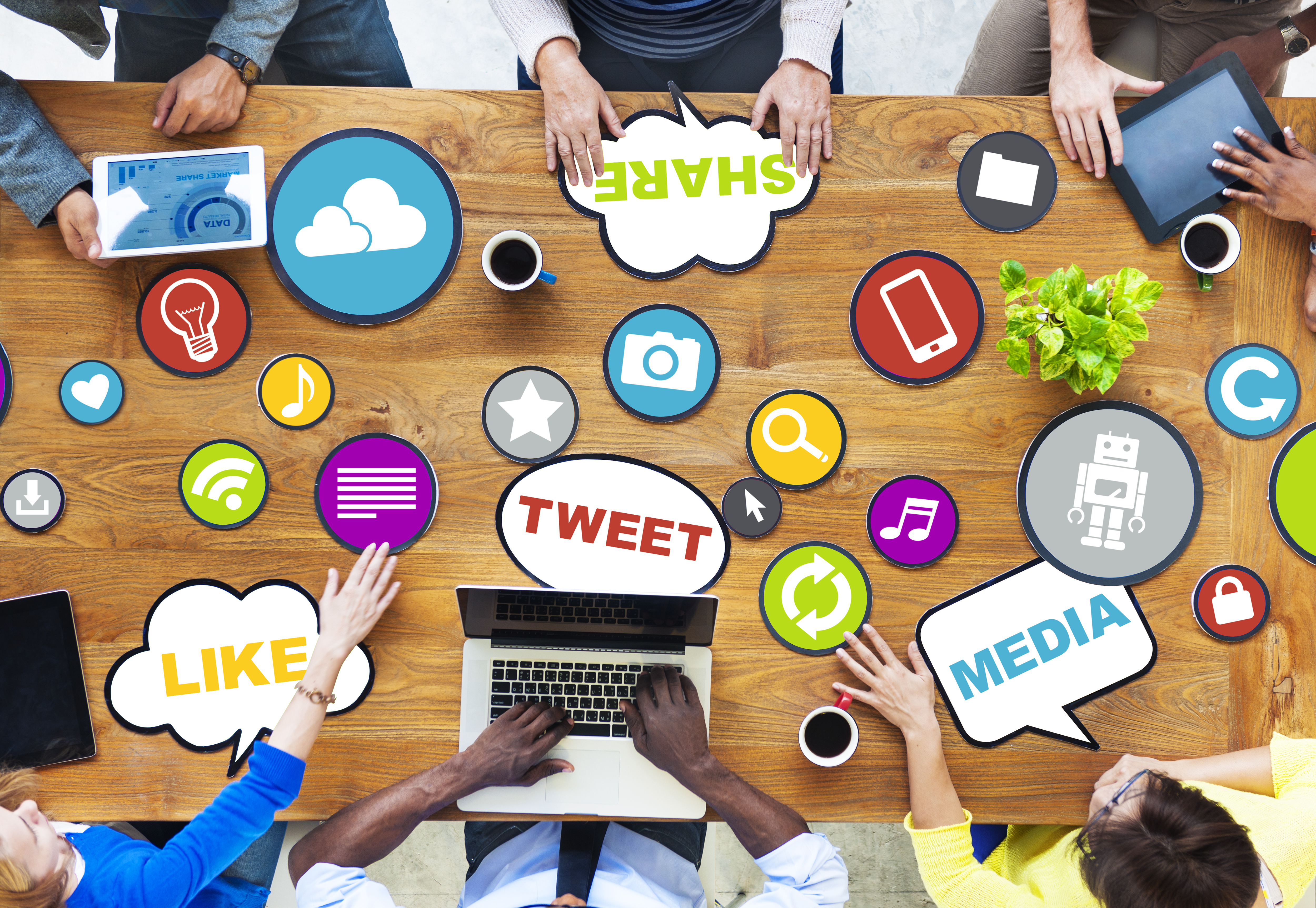 photo of people working at a table on various digital devices overlayed with digital media symbols and words